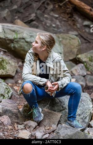 Ritratto di una ragazza pre-teen seduta su rocce in una zona rocciosa in un parco; Salmon Arm, British Columbia, Canada Foto Stock
