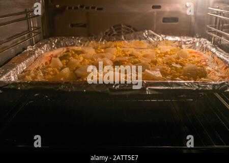 Pizza fatta in casa con ananas, sottaceti e mais nel forno Foto Stock