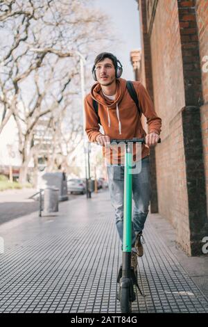 Ritratto di giovane uomo latino che guida scooter elettrico sulla strada della città. Concetto di trasporto moderno ed ecologico. Foto Stock