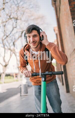 Ritratto di giovane uomo latino che guida scooter elettrico sulla strada della città. Concetto di trasporto moderno ed ecologico. Foto Stock