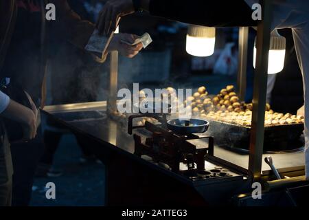 Uomo che vende mais bollito e castagne nel carrello. Fotografato in serata. Chiudi Foto Stock