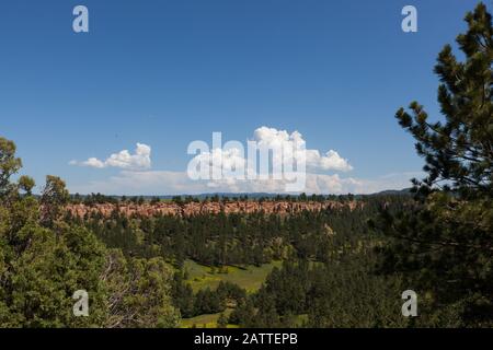 Guardando a sud-est della Devils Tower National Monument ad un bellissimo paesaggio di alberi in una valle verde e una scogliera di roccia rossa sedimentaria con un dis Foto Stock