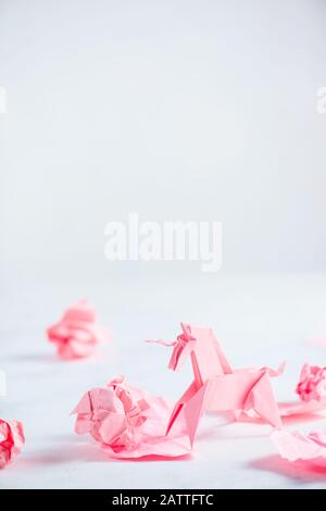 Unicorno di origami rosa con palline di carta sbriciolate. Processo creativo è scrittura, sfondo chiaro Foto Stock