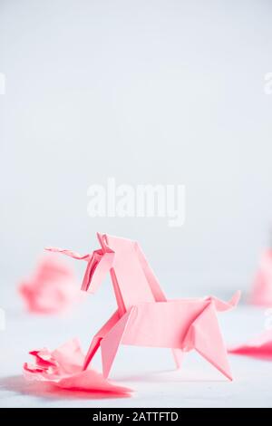 Unicorno di origami rosa con palline di carta sbriciolate. Processo creativo è scrittura, sfondo chiaro Foto Stock