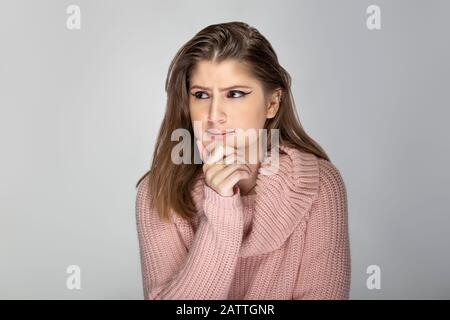 Primo piano ritratto di una giovane donna caucasica indossando un maglione rosa su sfondo grigio. Il modello sembra stressato e preoccupato Foto Stock
