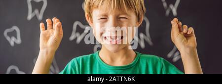 Il ragazzo caucasico little tiene un dente di latte caduto fra le sue dita e ride guardando nella BANDIERA della macchina fotografica, FORMATO LUNGO Foto Stock