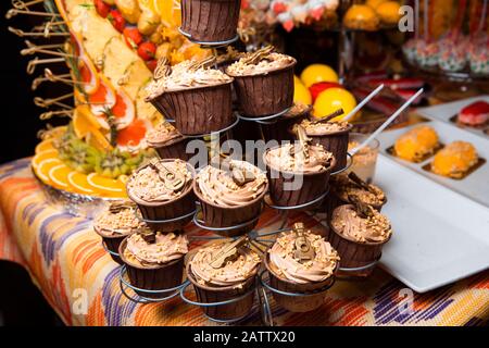 Torte al cioccolato appena fatte, decorate con crema e palline, stand su uno stand. Atmosfera di vacanza, dolce appetitoso. Candy bar. Foto Stock