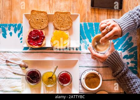 Primo piano vista del tavolo con cibo sano e donna adulta che fa colazione - marmellate frutta e tempo di caffè - immagine colorata del risveglio mattutino c Foto Stock
