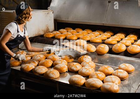 Una panetteria ragazza prende un pane pala di legno da un forno industriale in una panetteria. Produzione di pane industriale Foto Stock