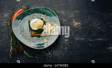 Colazione. Pane Tostato Con Spinaci, Uovo In Camicia E Parmigiano. Su uno sfondo di legno nero. Spazio di copia. Foto Stock