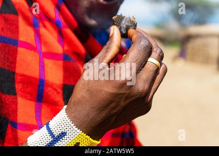 Uomo africano che tiene in mano una torta smoldering con bracciale colorato. Tanzania, Africa. Foto Stock