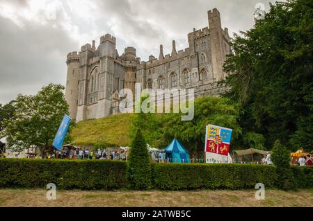 Il castello di Arundel si trova in cima a un rampart con persone che visitano le bancarelle del parco durante un festival medievale nel mese di luglio 2016. Foto Stock