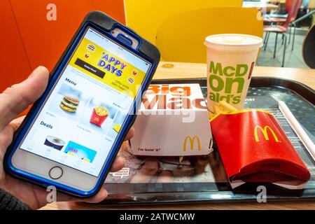 Una mano che tiene un telefono mobile con l'app McDonalds di fronte ad un pasto di un grande Mac in un ristorante veloce di <cDonalds. Foto Stock