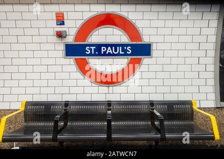 Un simbolo della metropolitana di Londra sul muro della stazione di St Paul sopra una fila di posti a sedere. Foto Stock