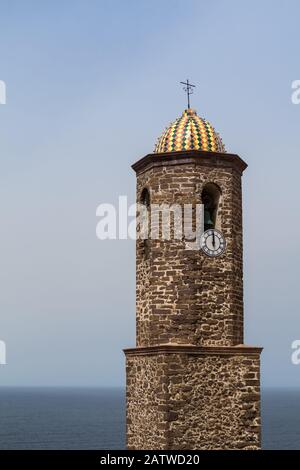 Cupola colorata in una torre di una chiesa di Sant'Antonio a Castelsardo, Sardegna, Italia. Orizzonte del mare mediterraneo e cielo blu sullo sfondo. Foto Stock