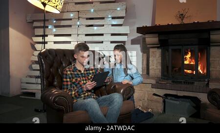 Piccola ragazza che disturba suo fratello per usare la compressa. Trascorrono del tempo in un accogliente soggiorno con grande camino Foto Stock