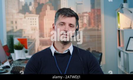 Ritratto di giovane caucasico che parla con la macchina fotografica in un call center. Ci sono grattacieli sullo sfondo. Foto Stock