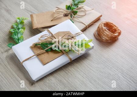 Composizione con scatole da regalo in stile naturale, elementi decorativi floreali e arco rustico a spago su sfondo in legno. Foto Stock