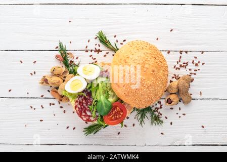 Hamburger, sandwich con salame, uova di quaglia e pomodori ciliegini. Su uno sfondo di legno. Vista dall'alto. Spazio di copia. Foto Stock