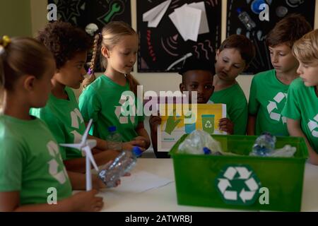 Gruppo di scolaresche che indossano t shirt verdi con un logo di riciclaggio bianco su di loro in piedi intorno ad un Foto Stock