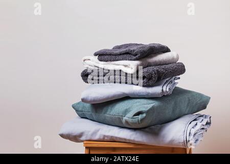 Pile di articoli tessili per la casa piegati e puliti vicino alla parete bianca. Casa accogliente, cameriere e stiratura Foto Stock