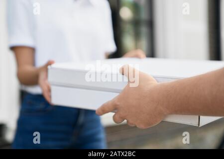 Fuoco selettivo delle mani maschili che danno due scatole di pizza alla donna. Primo piano di donna in incognito in abito casual che riceve ordine da liberyman all'aperto. Concetto di consegna di cibo. Foto Stock