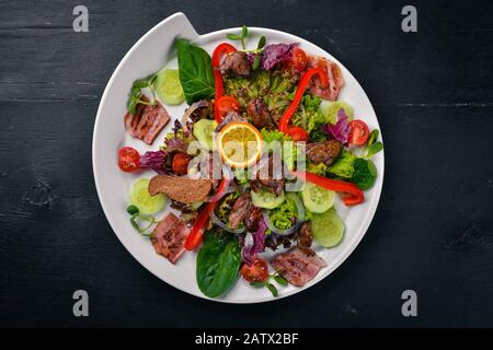 Insalata con pancetta e fegato di pollo. Su una superficie di legno. Vista dall'alto. Spazio libero per il testo. Foto Stock