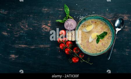 Zuppa cremosa con pancetta, uova di pollo, verdure e basilico. Su un tavolo di legno. Vista dall'alto. Spazio di copia. Foto Stock