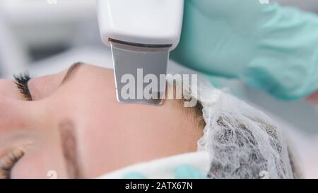 Il cosmetologo femminile esegue una procedura di pulizia a ultrasuoni viso, primo piano. Giovane donna in un salone di bellezza. Concetto di cosmetologia e professio Foto Stock