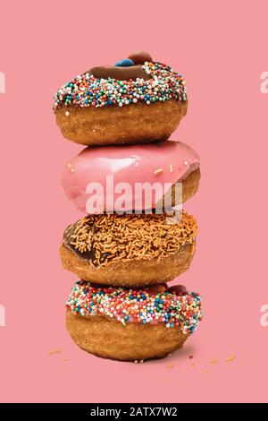 Ciambelle una sull'altra con glassa e cioccolato su sfondo rosa. Ciambelle dolci. Foto Stock