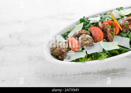 Insalata con fegato d'oca, spinaci, pomodori e parmigiano. Su uno sfondo di legno. Vista dall'alto. Spazio libero di copia Foto Stock