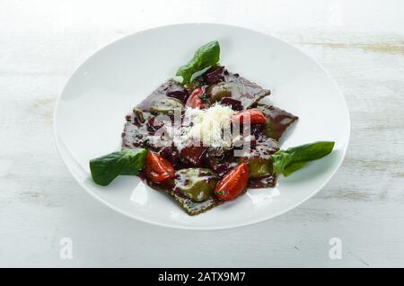 Ravioli con spinaci, funghi e salsa di vino rosso. In un piatto su uno sfondo di legno. Vista dall'alto. Spazio libero di copia. Foto Stock