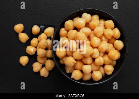 Ceci cotti in una ciotola in ceramica nera isolata su legno verniciato nero. Ceci rovesciati. Vista dall'alto. Foto Stock