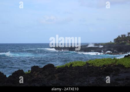 Onde che si infrangono nella costa rocciosa e vulcanica della baia nel Waianapanapa state Park, Hana, Maui, Hawaii, USA Foto Stock