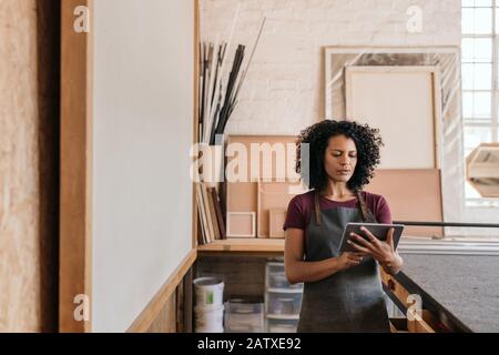 Giovane donna che usa un tablet nel suo laboratorio di incorniciatura Foto Stock