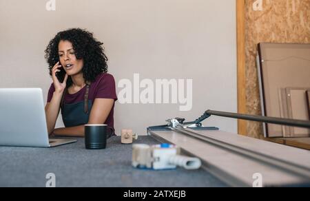 Giovane donna che parla al telefono nel suo laboratorio di incorniciatura Foto Stock