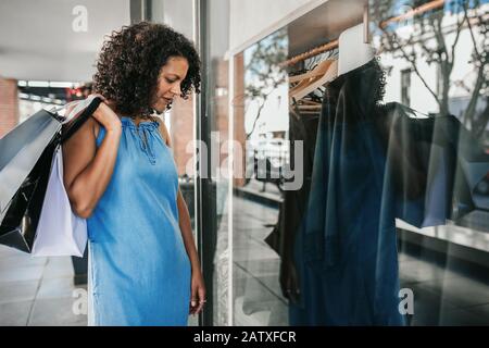 Donna sorridente che guarda i vestiti in una finestra boutique Foto Stock