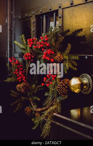 Un giuramento fatto a mano di rami di abete, bacche di oly e coni di pino sulla porta ad un luogo di evento a Natale Foto Stock