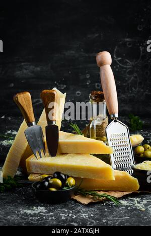Set di formaggi a pasta dura con coltelli da formaggio su fondo in pietra nera. Parmigiano. Vista dall'alto. Spazio libero per il testo. Foto Stock