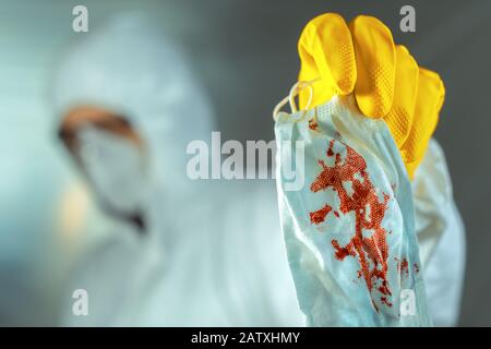 Operatore medico che smaltisce la maschera respiratoria protettiva sanguinosa in quarantena, messa a fuoco selettiva Foto Stock