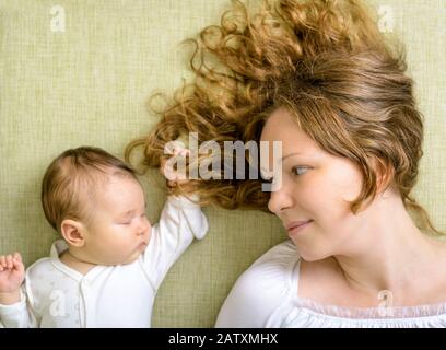 Bella donna guarda la sua figlia neonato sul divano a casa Foto Stock