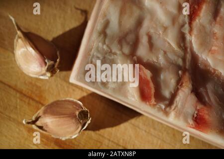 Sul tavolo si trova un pezzo di lardo intero e due spicchi d'aglio Foto Stock