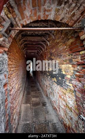 Vecchia strada stretta a Venezia, Italia. Vicolo medievale tra le case. Strada coperta di mattoni come un tunnel. Vecchio passaggio nella città antica. Il buio vintage Foto Stock