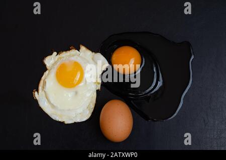 Uovo di pollo intero, uovo crudo rotto e fritto su sfondo nero. Tre stati diversi di un prodotto. Vista dall'alto. Messa a fuoco selettiva. Foto Stock