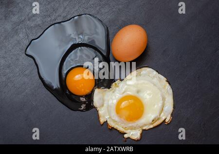 Uovo di pollo intero, uovo crudo rotto e fritto su sfondo nero. Tre stati diversi di un prodotto. Vista dall'alto. Messa a fuoco selettiva. Orizzontale Foto Stock