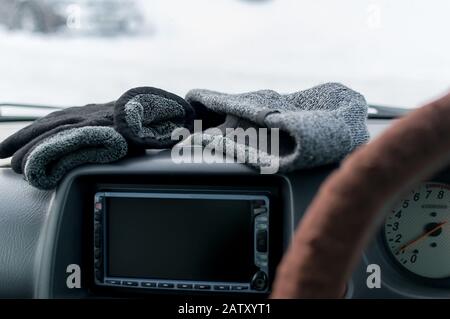 primo piano, guanti invernali caldi e un cappello si trovano sul pannello dell'auto Foto Stock