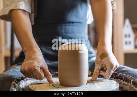 Donna vasaio che lavora su una ruota di Potter che fa un vaso. Master tira la brocca fuori dal cerchio bagnandola con acqua e tenendola delicatamente nelle mani. Clos Foto Stock