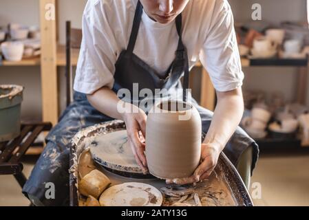 Donna vasaio che lavora su una ruota di Potter che fa un vaso. Master tira la brocca fuori dal cerchio bagnandola con acqua e tenendola delicatamente nelle mani Foto Stock