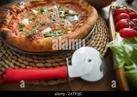 Primo piano di pizza fatta in casa con coltello speciale sul tavolo di legno servito per cena Foto Stock