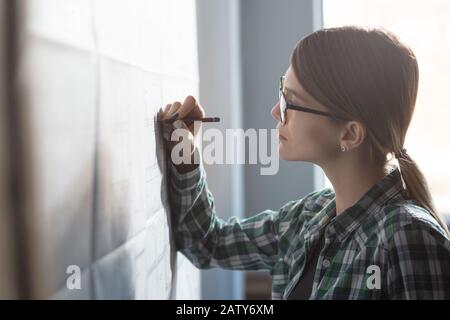 Primo piano ritratto di bella donna concentrato sul lavoro. Architetto che lavora in ufficio con progetti. Progettazione di un progetto di costruzione. Arco Foto Stock